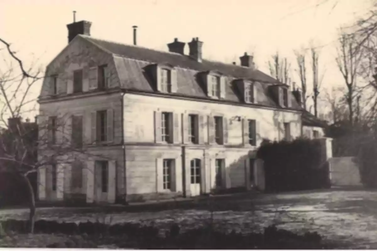 Old black-and-white photograph of a large two-story house with a sloped roof and several chimneys, surrounded by leafless trees. Old black-and-white photograph of a large two-story house with a sloped roof and several chimneys, surrounded by leafless trees.