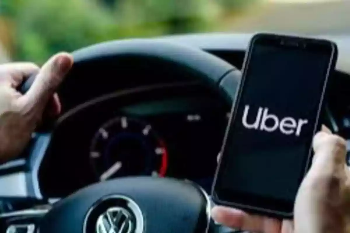 Persona sosteniendo un teléfono móvil con la aplicación de Uber abierta mientras conduce un automóvil Volkswagen Persona sosteniendo un teléfono móvil con la aplicación de Uber abierta mientras conduce un automóvil Volkswagen