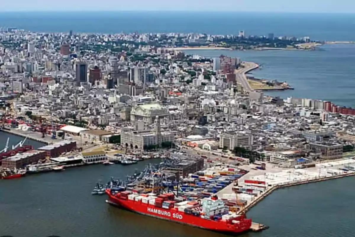Vista aérea de un puerto con un gran barco de carga rojo y una ciudad costera al fondo