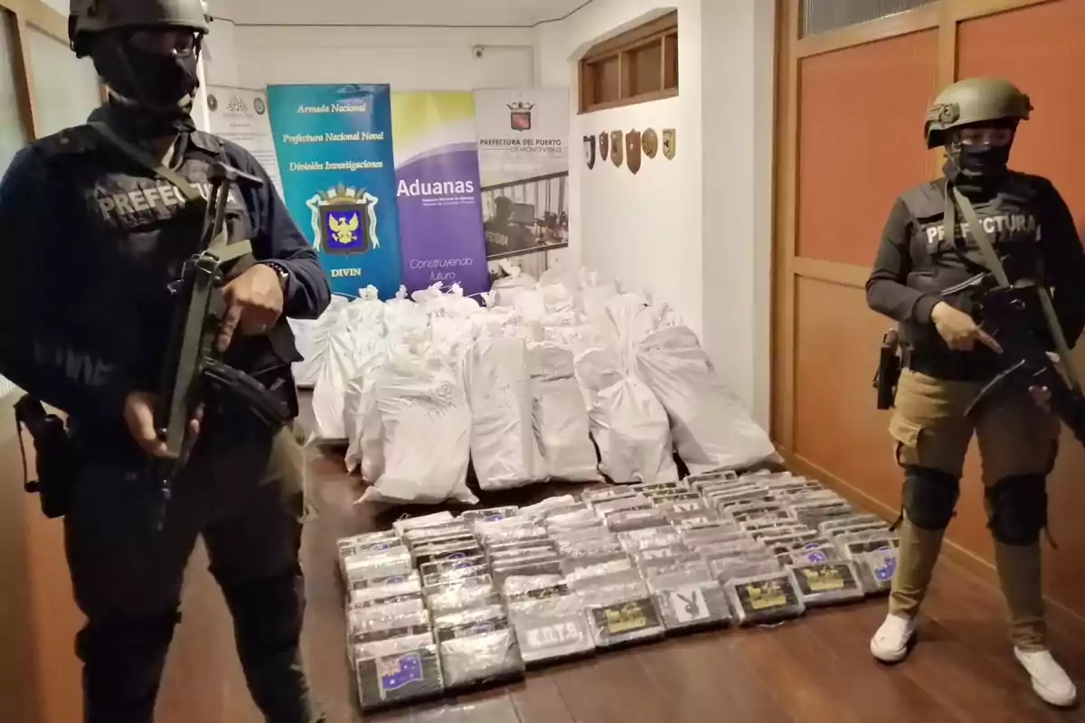 Two armed, hooded agents guard numerous packages and white bags stacked in a room, with official signs in the background. Two armed, hooded agents guard numerous packages and white bags stacked in a room, with official signs in the background.
