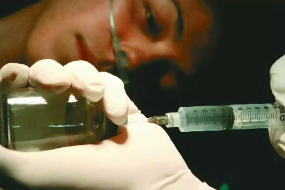 Person wearing medical gloves filling a syringe with liquid from a vial while closely observing. Person wearing medical gloves filling a syringe with liquid from a vial while closely observing.