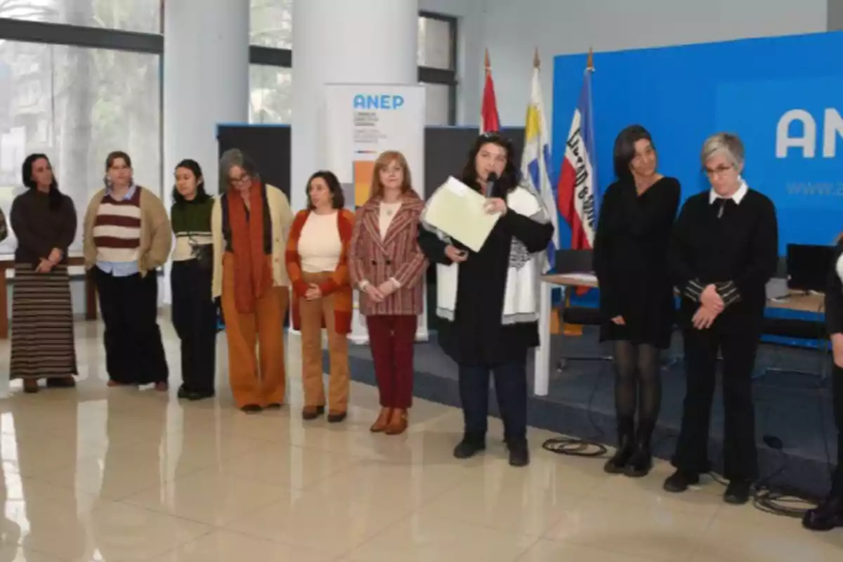A group of women is standing in line inside a room with a tiled floor, some of them holding papers, and in the background there are flags and an ANEP sign. A group of women is standing in line inside a room with a tiled floor, some of them holding papers, and in the background there are flags and an ANEP sign.