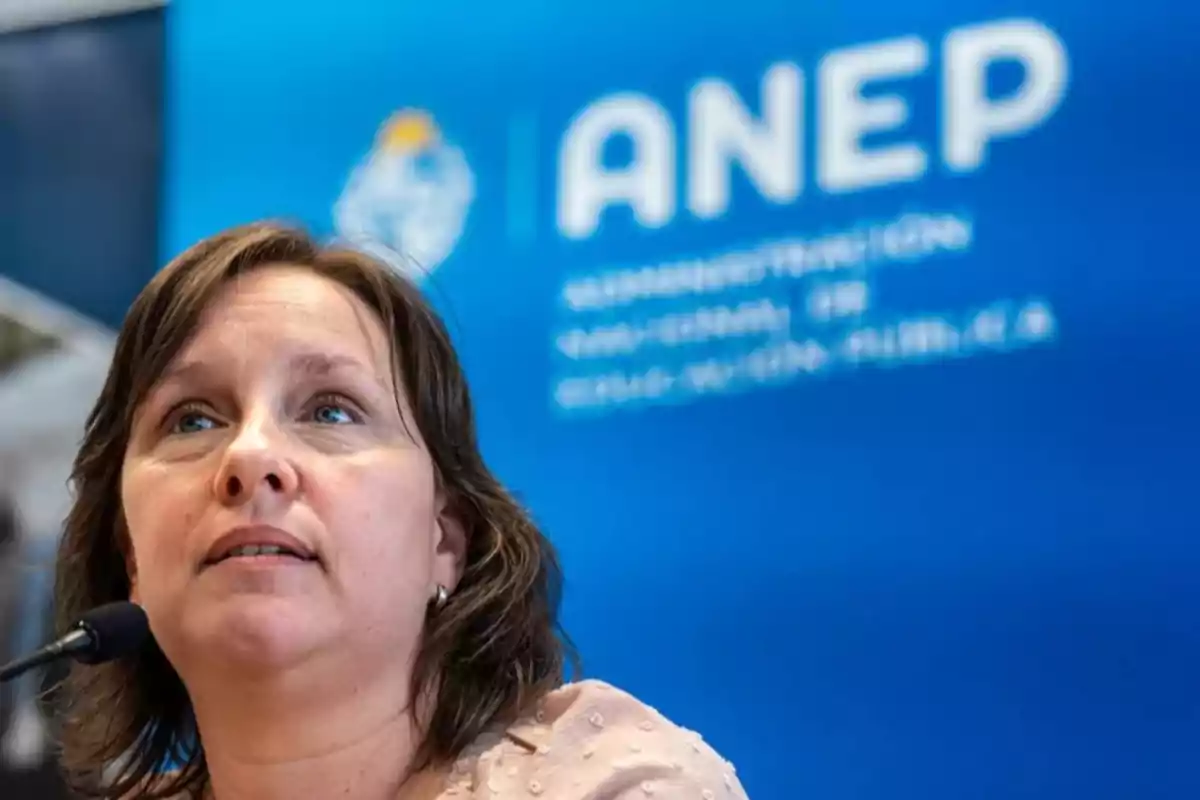 Woman speaking in front of a microphone with a blue sign in the background that says ANEP Woman speaking in front of a microphone with a blue sign in the background that says ANEP