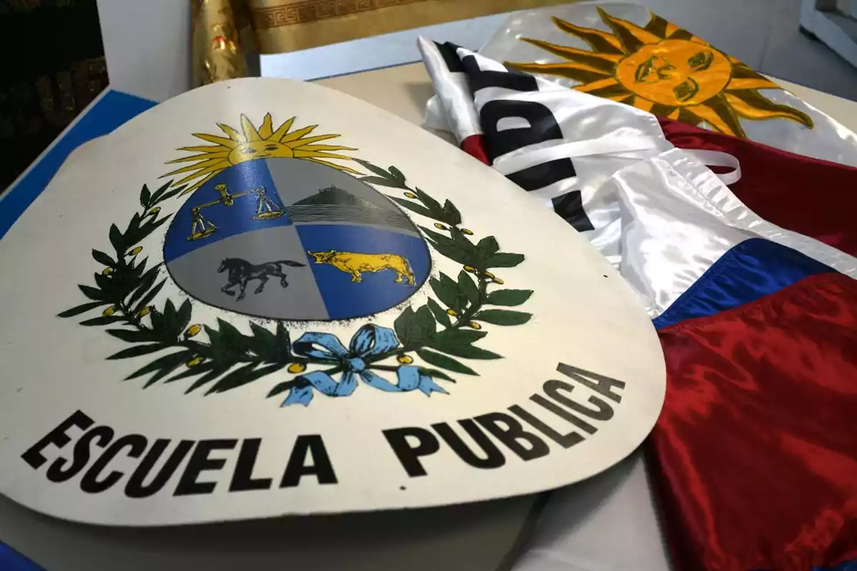 Coat of arms of Uruguay with the inscription Public School next to a folded Uruguayan flag on a table