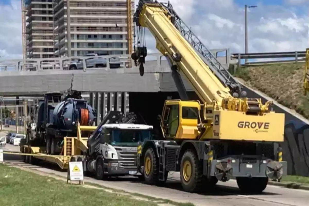 Grúa amarilla asistiendo a un camión atascado bajo un puente en una zona urbana