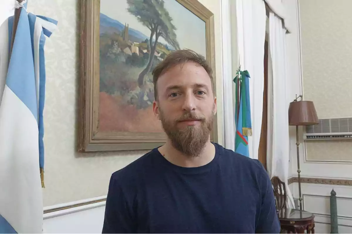 Bearded man in a dark jersey posing in an office with flags and a landscape painting in the background Bearded man in a dark jersey posing in an office with flags and a landscape painting in the background