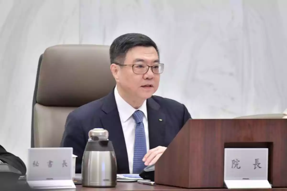 Man with glasses and a blue suit sitting at a meeting table next to a thermos and signs with Chinese characters Man with glasses and a blue suit sitting at a meeting table next to a thermos and signs with Chinese characters