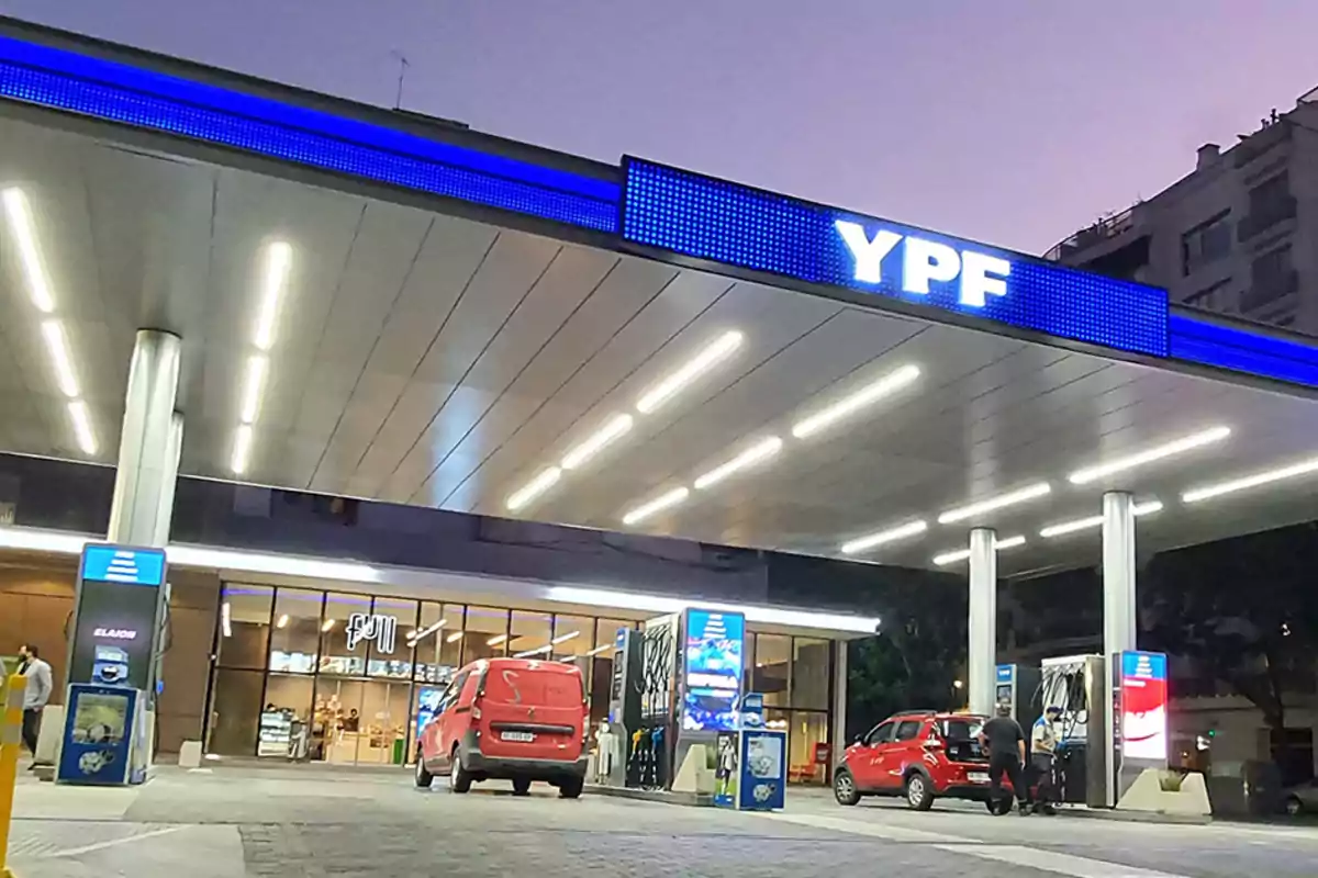 YPF gas station illuminated at dusk with red cars refueling and people near the pumps YPF gas station illuminated at dusk with red cars refueling and people near the pumps
