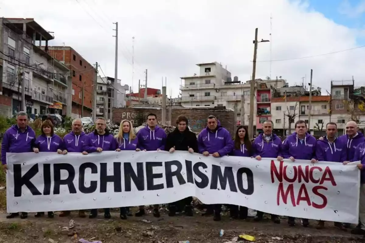 Un grupo de personas con camperas violetas sostiene una pancarta que dice Kirchnerismo nunca más en un barrio urbano con edificios de fondo