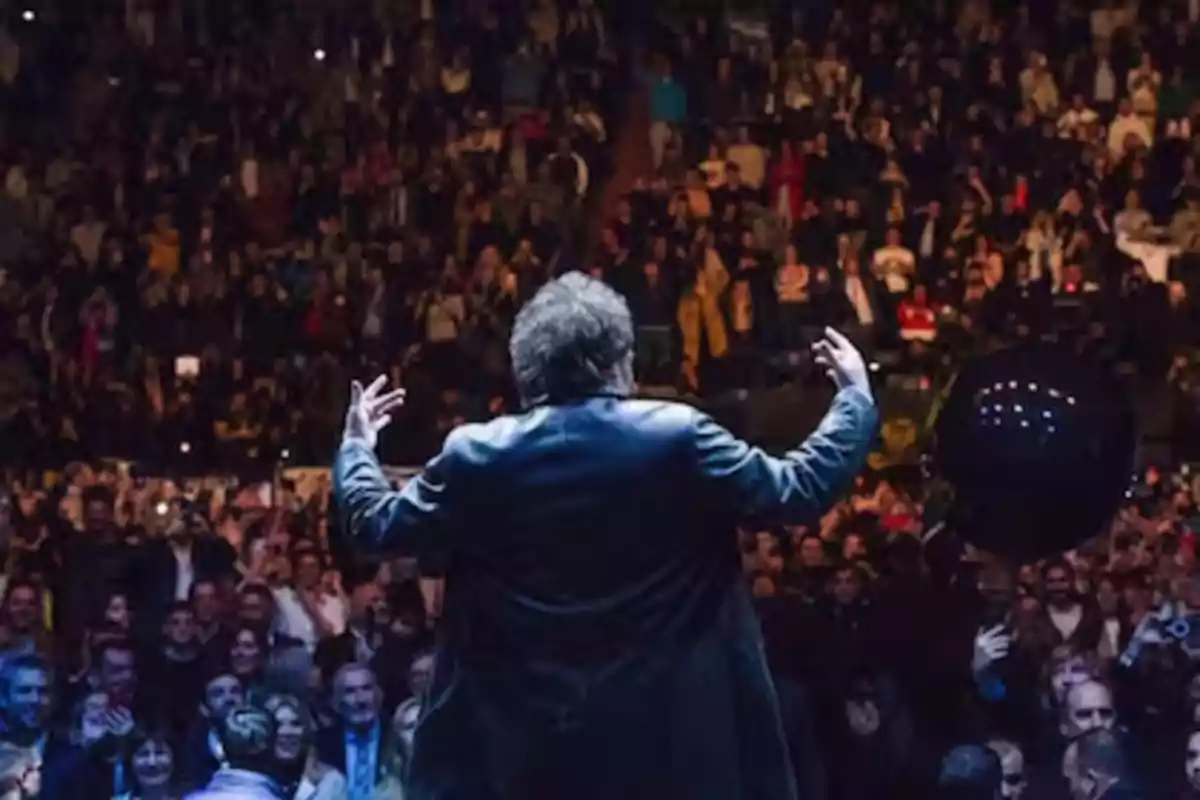 Person standing with their back to the audience on stage in front of a crowd in a packed auditorium