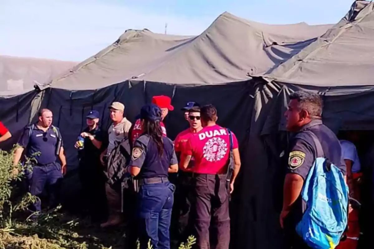 Varios rescatistas y personal de emergencia conversan frente a una carpa de campaña en un entorno al aire libre