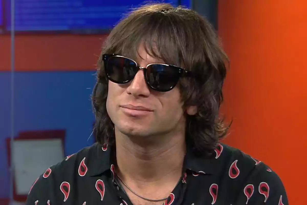 Hombre de cabello largo y gafas de sol con camisa negra estampada en un estudio de televisión Hombre de cabello largo y gafas de sol con camisa negra estampada en un estudio de televisión