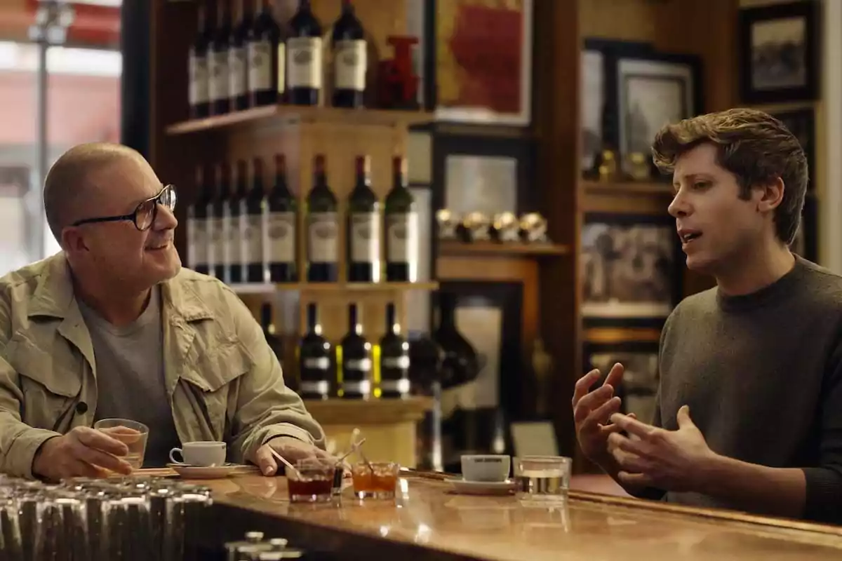 Dos hombres conversan sentados en la barra de un café rodeados de botellas de vino y tazas de café Dos hombres conversan sentados en la barra de un café rodeados de botellas de vino y tazas de café