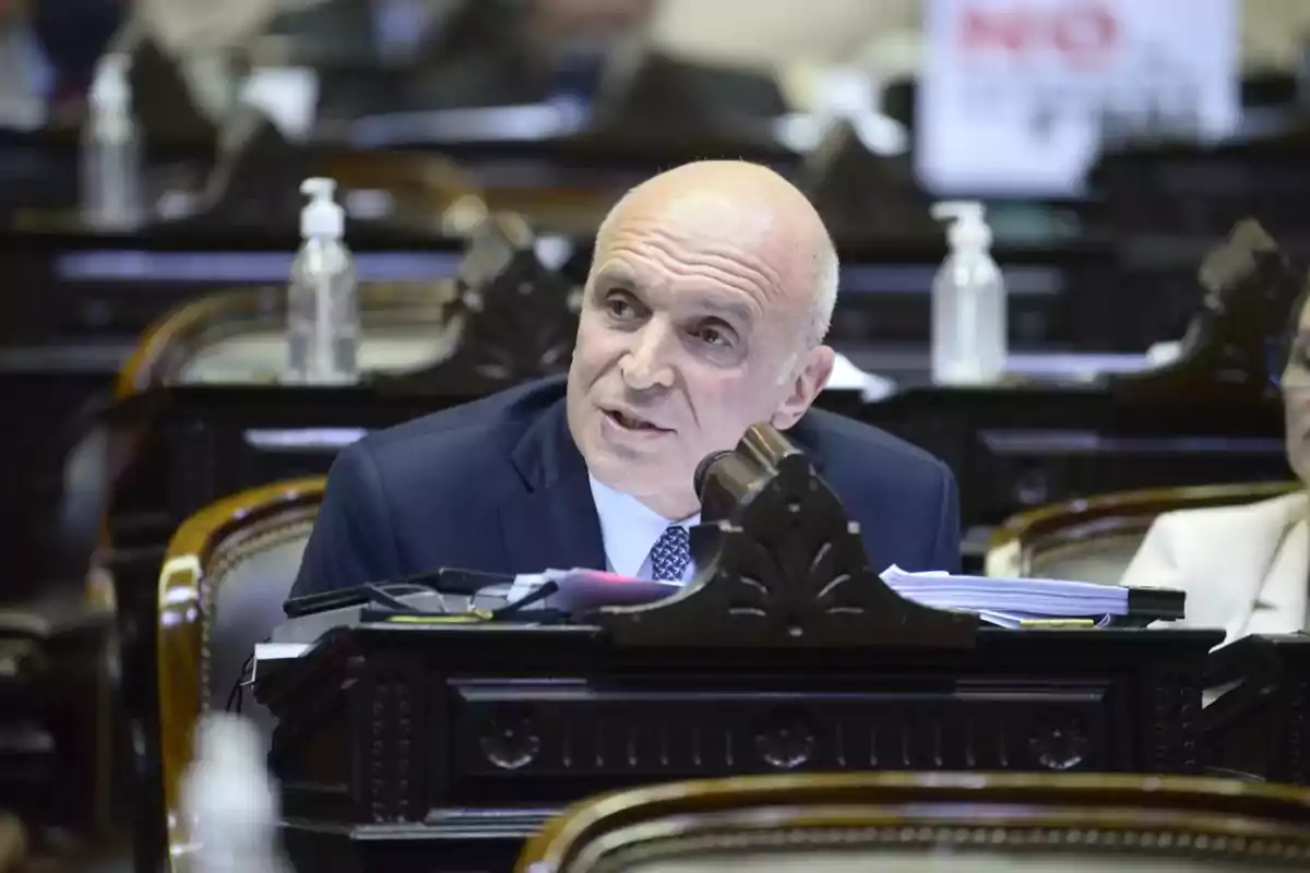 Bald man in a blue suit speaking into a microphone during a parliamentary session Bald man in a blue suit speaking into a microphone during a parliamentary session