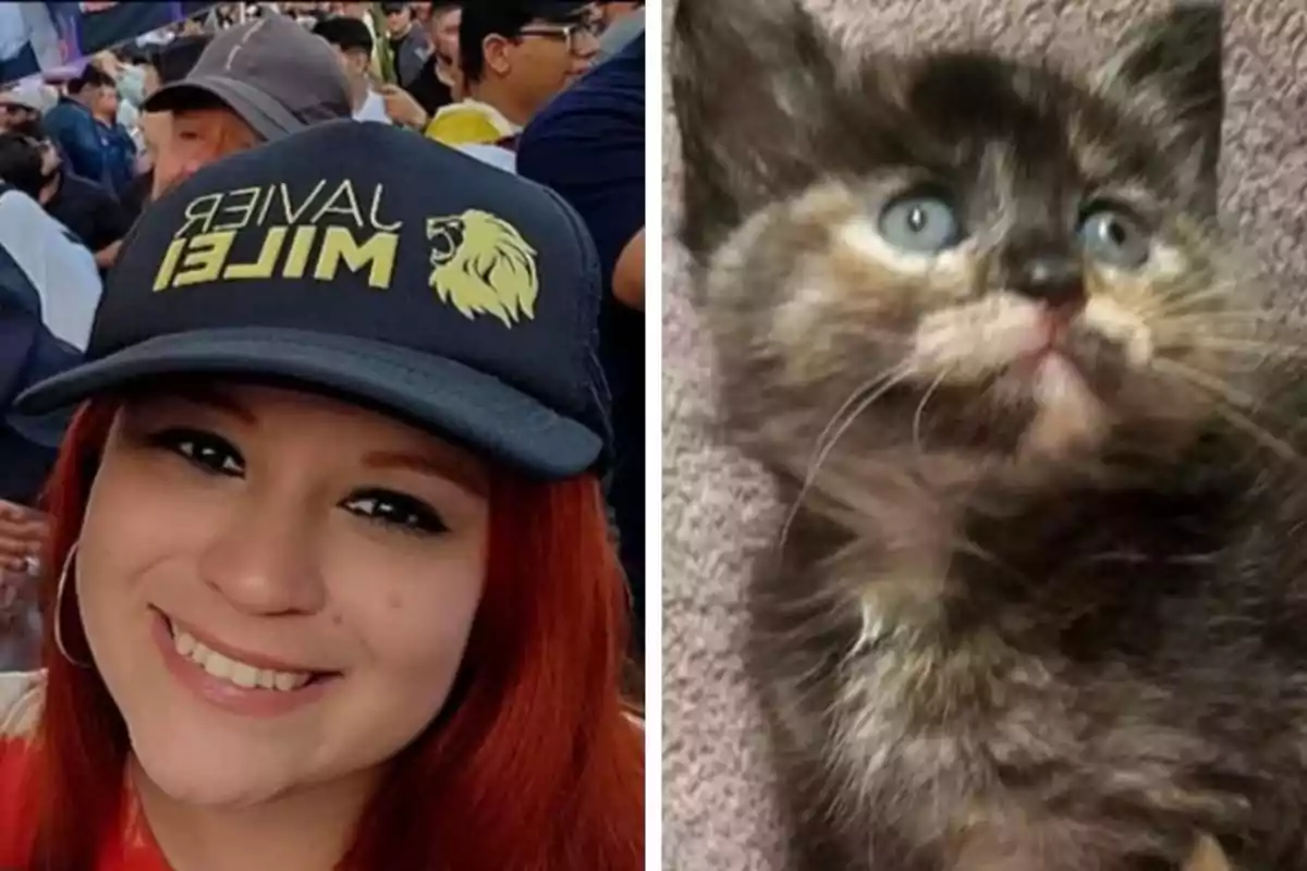 A red-haired woman smiles while wearing a black cap with yellow letters, as a dark-furred kitten with light spots and blue eyes looks up beside her.