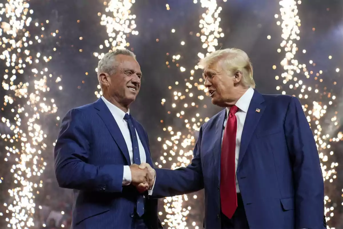 Dos hombres de traje se dan la mano mientras fuegos artificiales iluminan el fondo