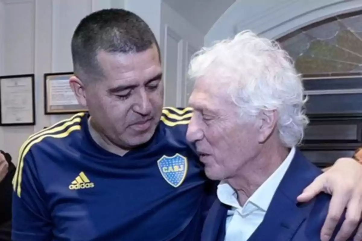 Dos hombres se abrazan y conversan en un ambiente interior uno lleva una camiseta azul de Boca Juniors y el otro viste un saco azul con camisa blanca Dos hombres se abrazan y conversan en un ambiente interior uno lleva una camiseta azul de Boca Juniors y el otro viste un saco azul con camisa blanca