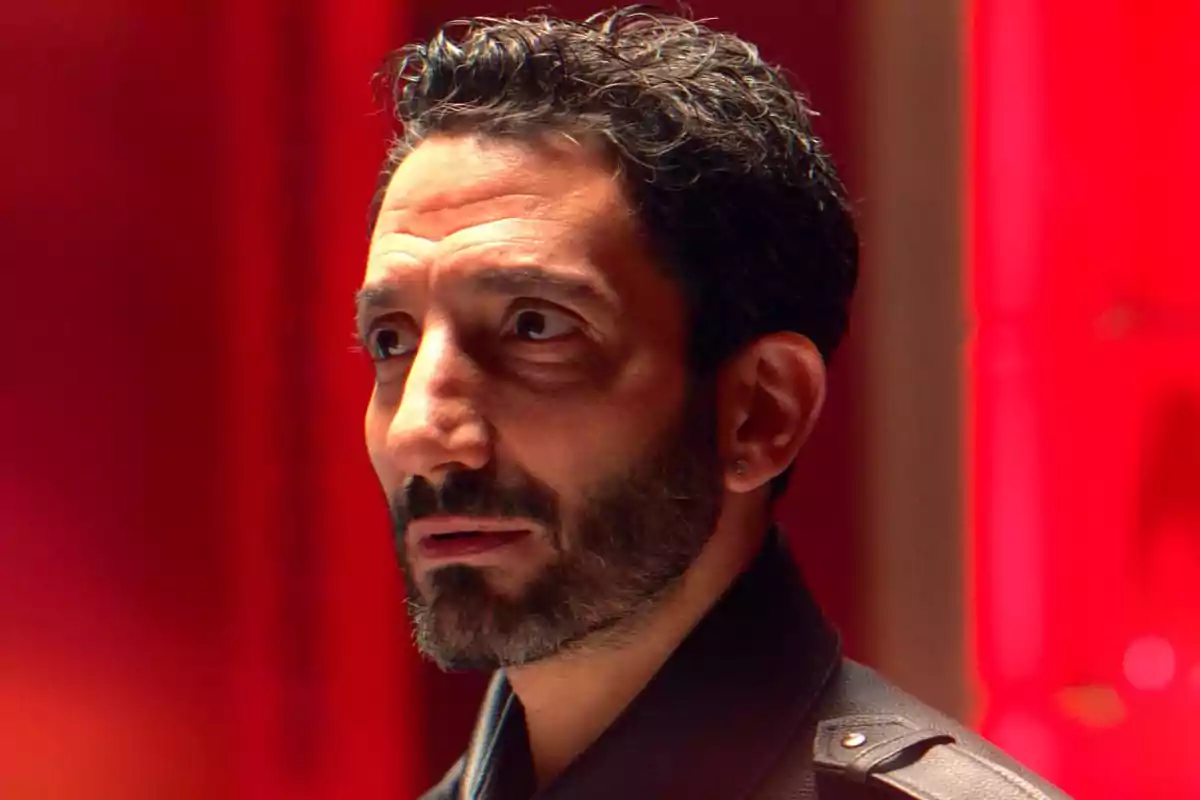 Hombre de cabello corto y barba mirando hacia un lado con expresión seria sobre un fondo rojo. Hombre de cabello corto y barba mirando hacia un lado con expresión seria sobre un fondo rojo.