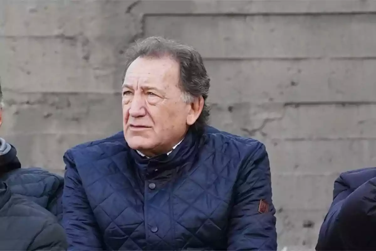 Older man in a blue jacket sitting in front of a concrete wall Older man in a blue jacket sitting in front of a concrete wall