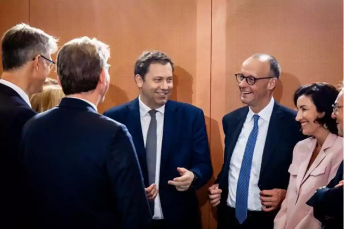 Grupo de personas vestidas de manera formal conversando y sonriendo en un ambiente interior.