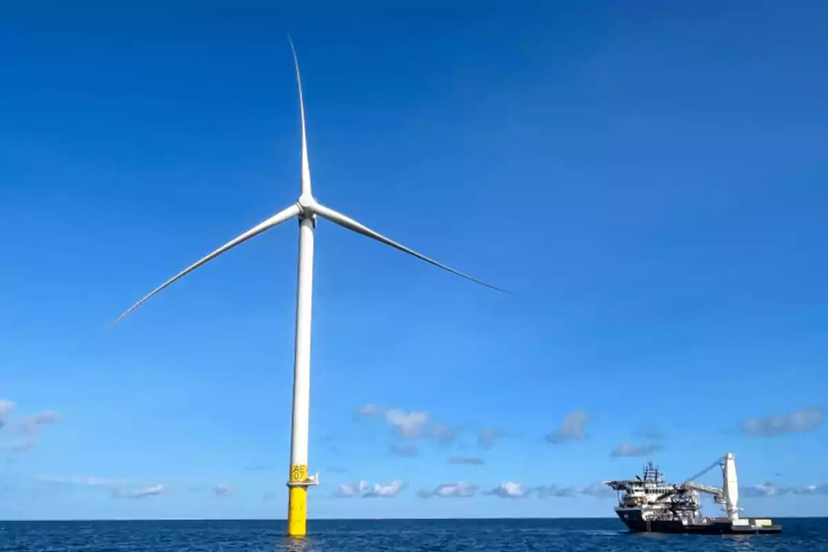 Offshore wind turbine next to a ship in the ocean under a clear sky Offshore wind turbine next to a ship in the ocean under a clear sky