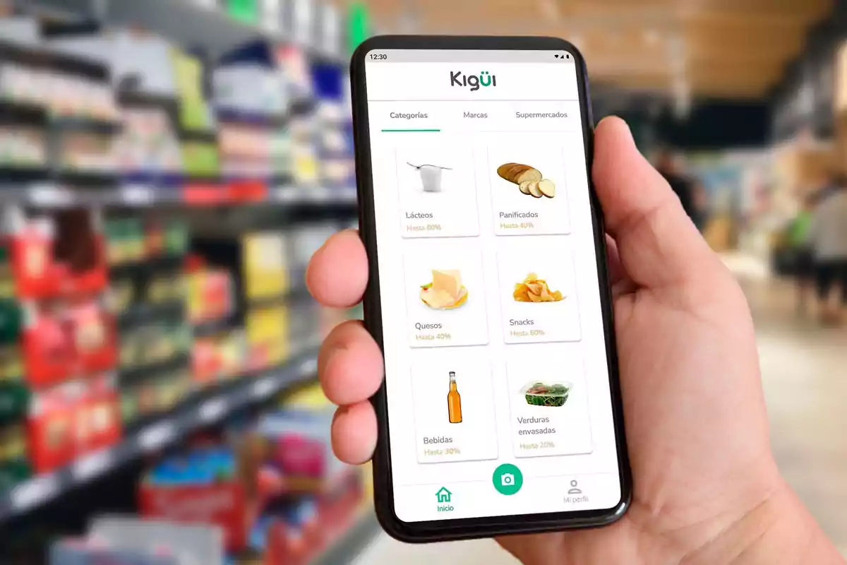 Persona sosteniendo un teléfono móvil que muestra una aplicación de compras con categorías de productos en un supermercado desenfocado de fondo Persona sosteniendo un teléfono móvil que muestra una aplicación de compras con categorías de productos en un supermercado desenfocado de fondo