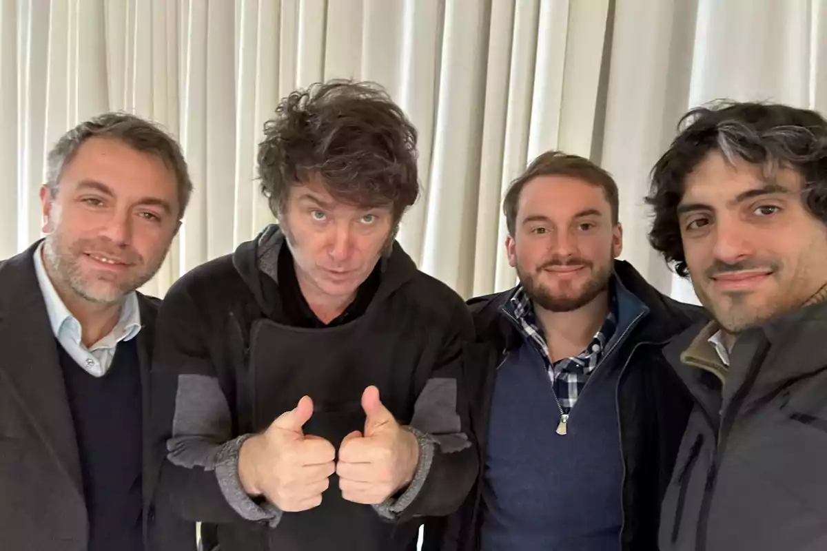 Four men pose together in front of a white curtain, the second from the left gives a thumbs-up gesture, and the others smile. Four men pose together in front of a white curtain, the second from the left gives a thumbs-up gesture, and the others smile.