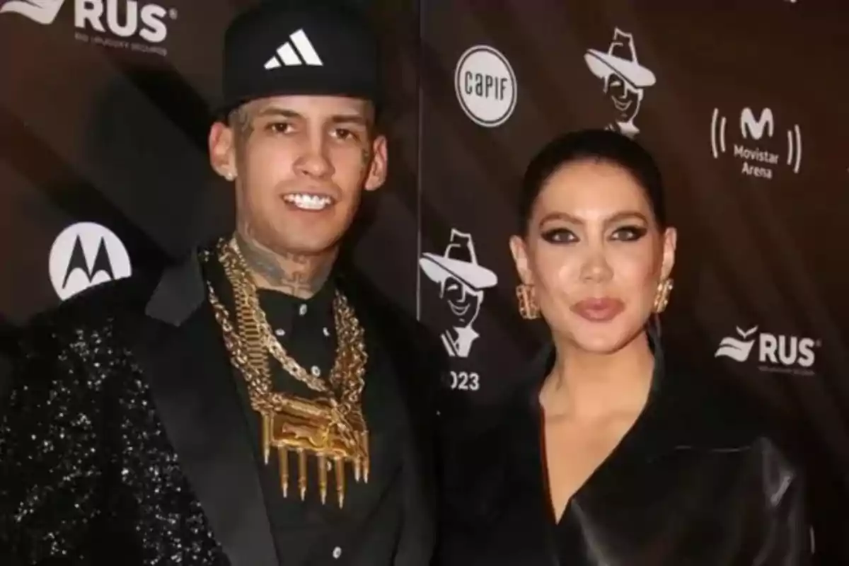 Two people pose together at an event with a backdrop of logos, both wearing elegant clothing and striking accessories. Two people pose together at an event with a backdrop of logos, both wearing elegant clothing and striking accessories.