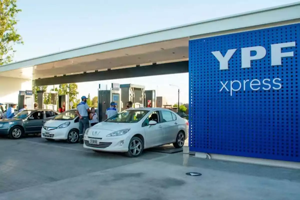 Cars lining up at a YPF xpress gas station with several people attending to customers