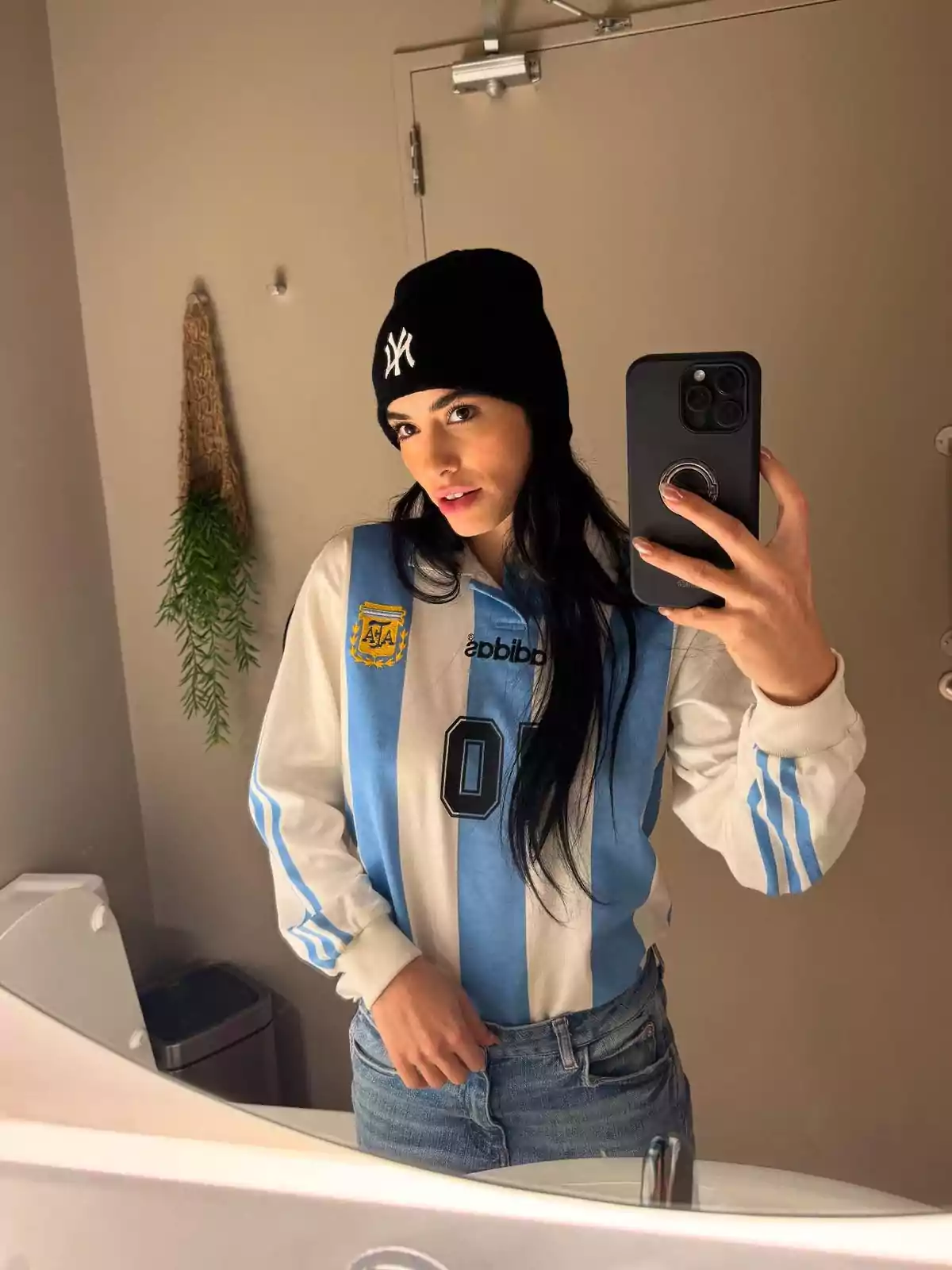 Mujer tomándose una selfie en el baño usando gorro negro y camiseta de la selección argentina de fútbol Mujer tomándose una selfie en el baño usando gorro negro y camiseta de la selección argentina de fútbol