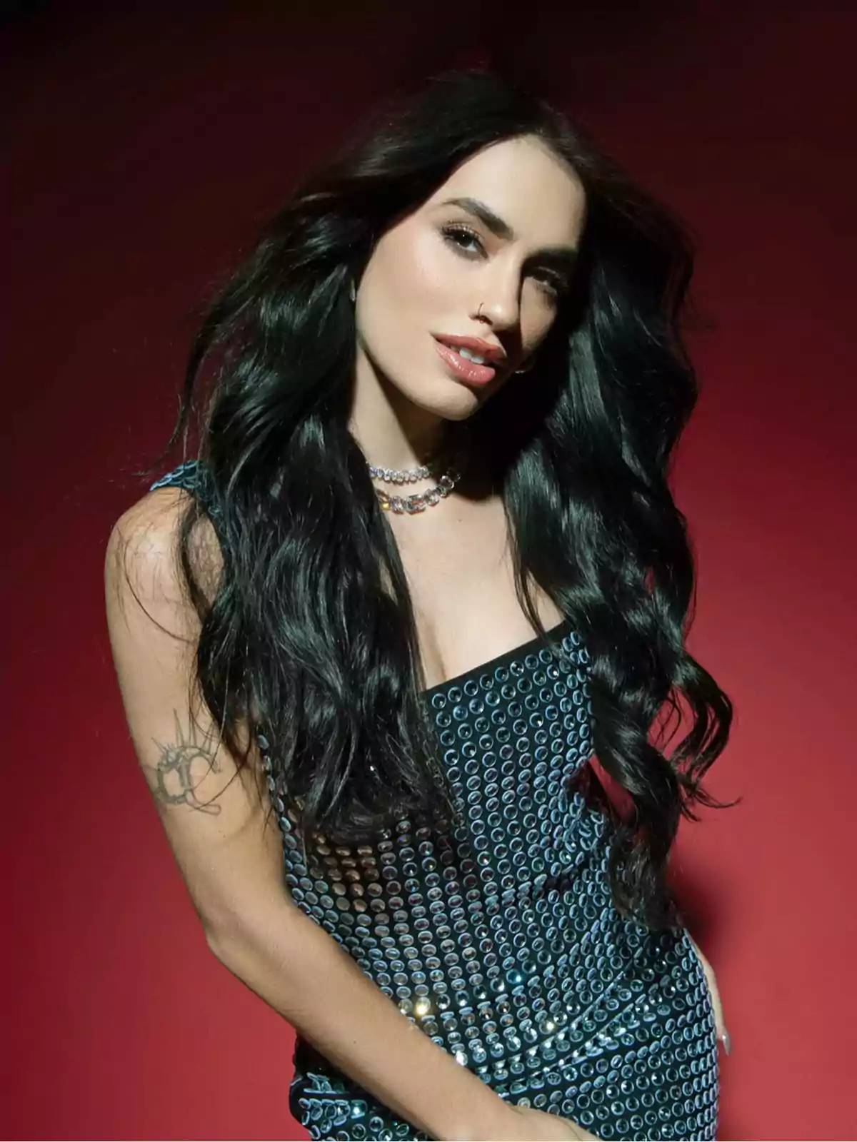Mujer de cabello largo y oscuro con vestido brillante posando frente a un fondo rojo Mujer de cabello largo y oscuro con vestido brillante posando frente a un fondo rojo