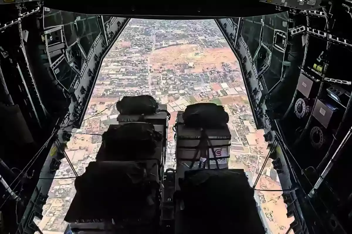 View from inside a military cargo plane with the rear ramp open and several boxes ready to be dropped over a city View from inside a military cargo plane with the rear ramp open and several boxes ready to be dropped over a city