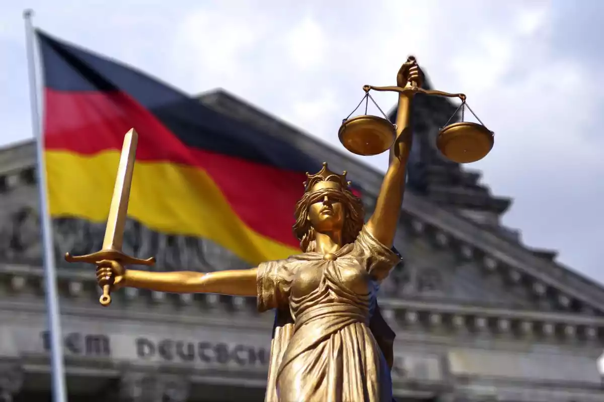 Golden statue of Justice with a scale and a sword in front of a building and a German flag waving in the background Golden statue of Justice with a scale and a sword in front of a building and a German flag waving in the background
