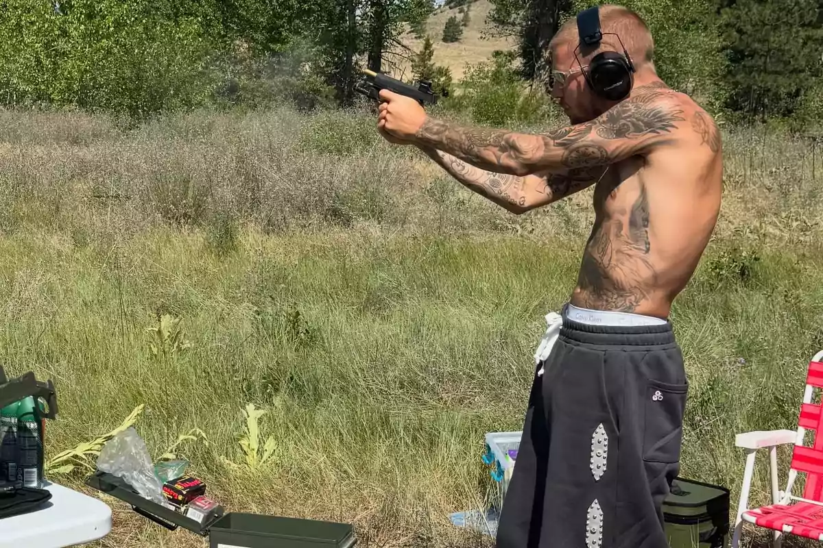 Shirtless man with tattoos shooting a gun in an open field while wearing hearing protection and safety glasses Shirtless man with tattoos shooting a gun in an open field while wearing hearing protection and safety glasses