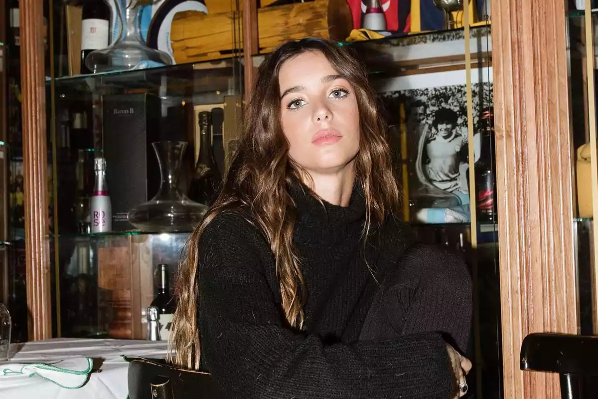 Long-haired woman with loose hair wearing a black sweater sitting in a restaurant with display cases in the background