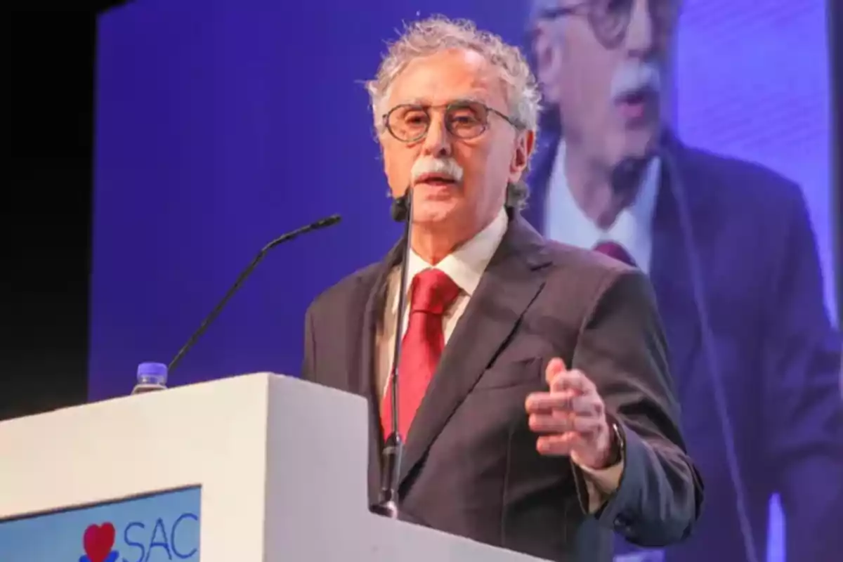 Hombre mayor con gafas y bigote hablando en un podio durante una conferencia profesional