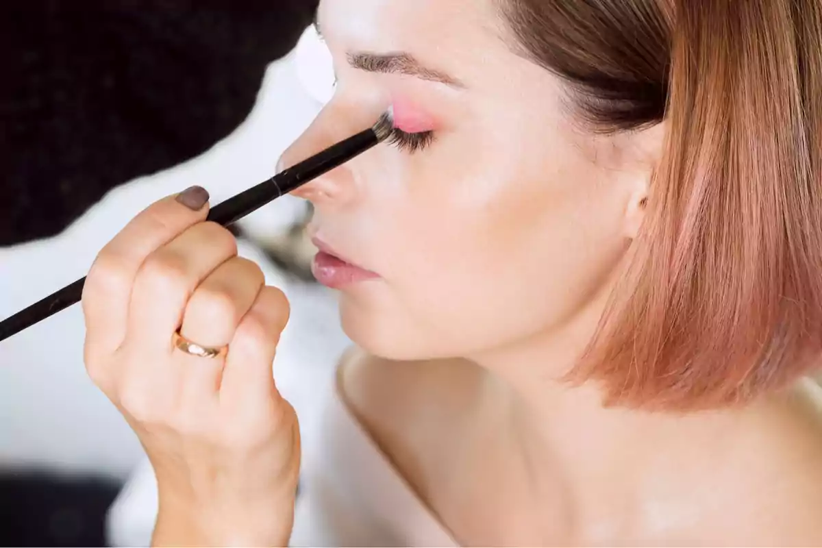 Mujer aplicándose sombra de ojos rosa con una brocha de maquillaje