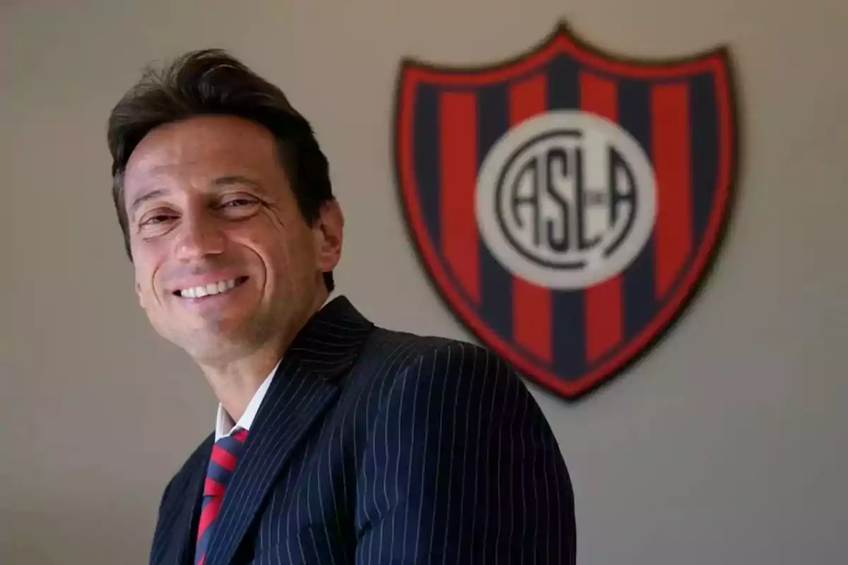 Smiling man in a suit and tie in front of a San Lorenzo de Almagro crest