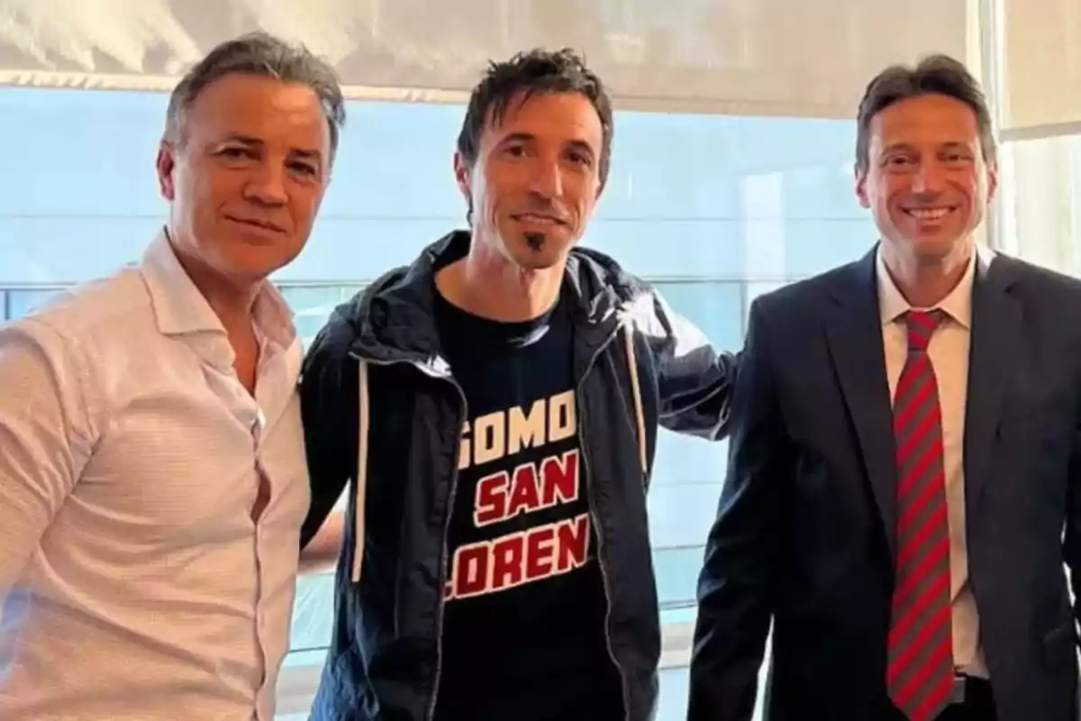 Three men pose together and smile in a well-lit indoor setting. Three men pose together and smile in a well-lit indoor setting.