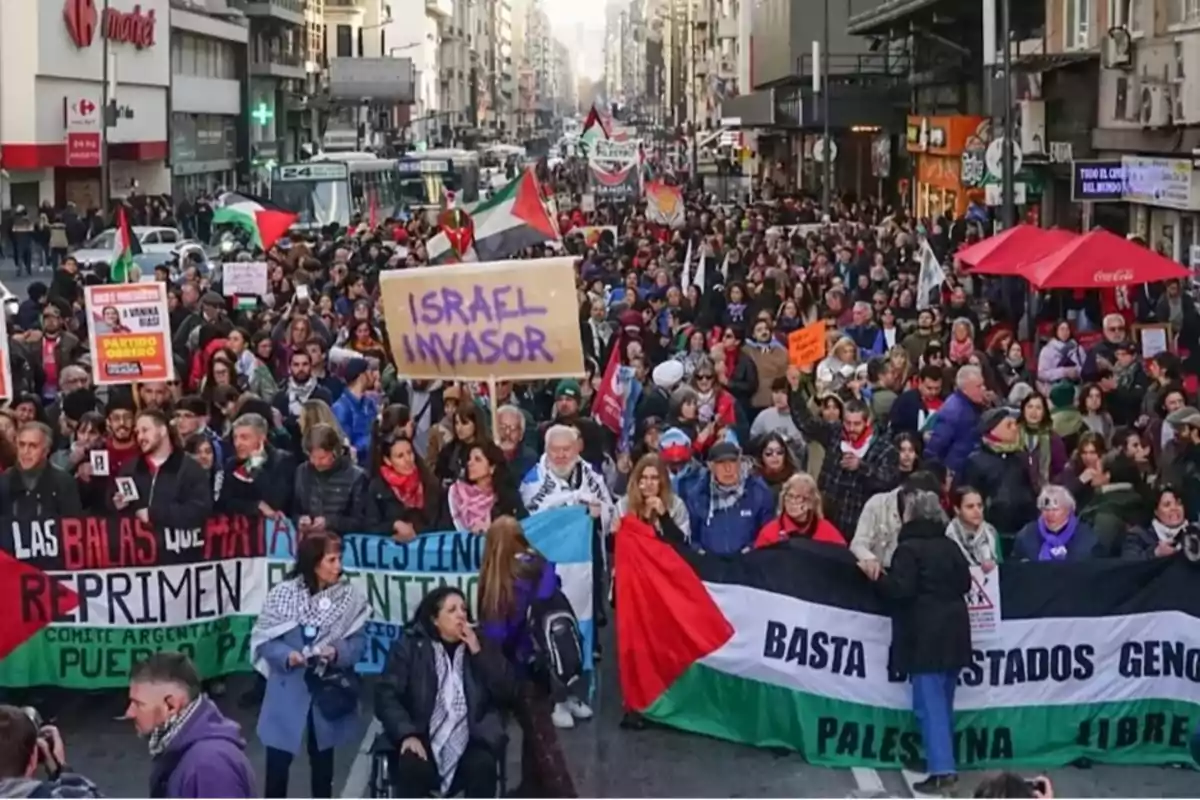 Manifestación multitudinaria en una calle de ciudad con personas sosteniendo pancartas y banderas en apoyo a Palestina