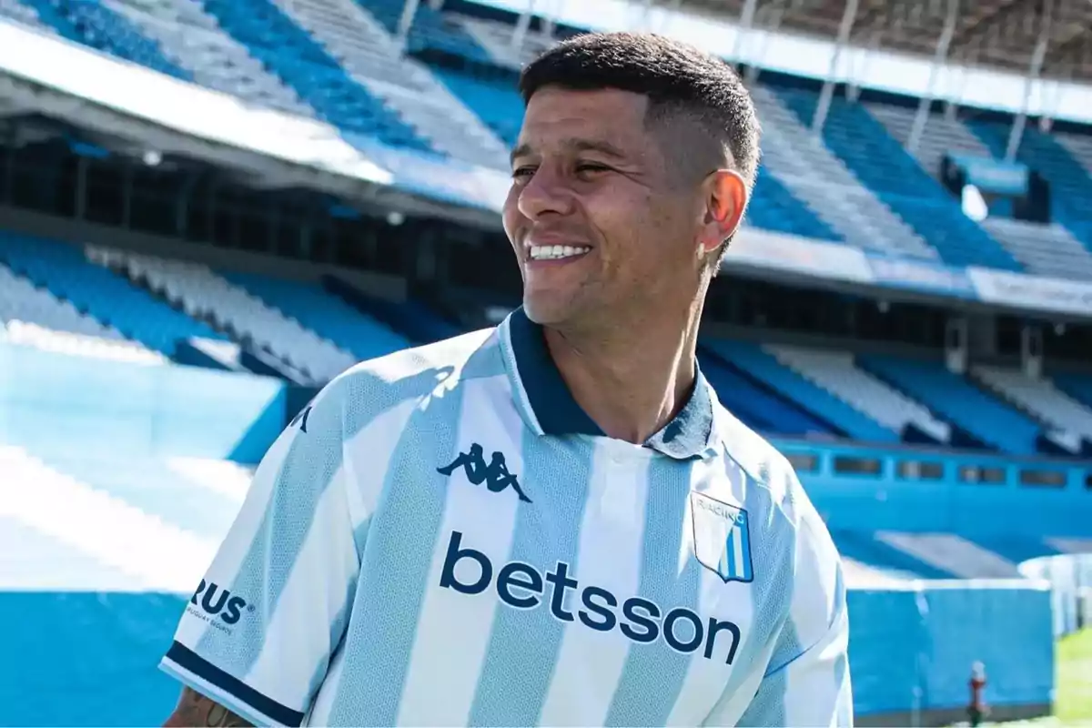Futbolista sonriente con la camiseta de Racing Club en un estadio vacío