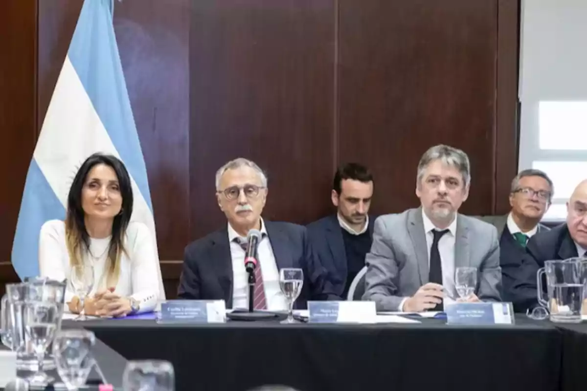 Several people sitting at a conference table with the Argentine flag in the background