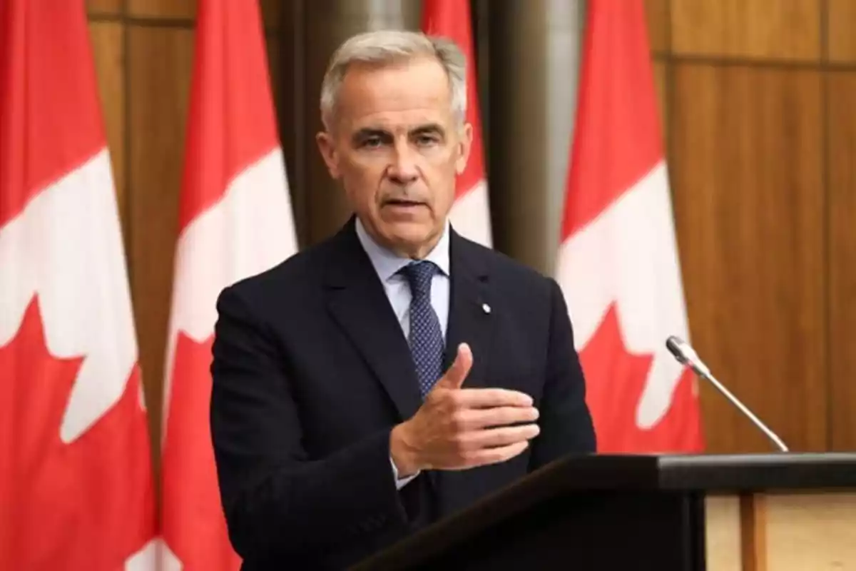 Hombre de cabello canoso con traje oscuro hablando en un podio frente a varias banderas de Canadá Hombre de cabello canoso con traje oscuro hablando en un podio frente a varias banderas de Canadá