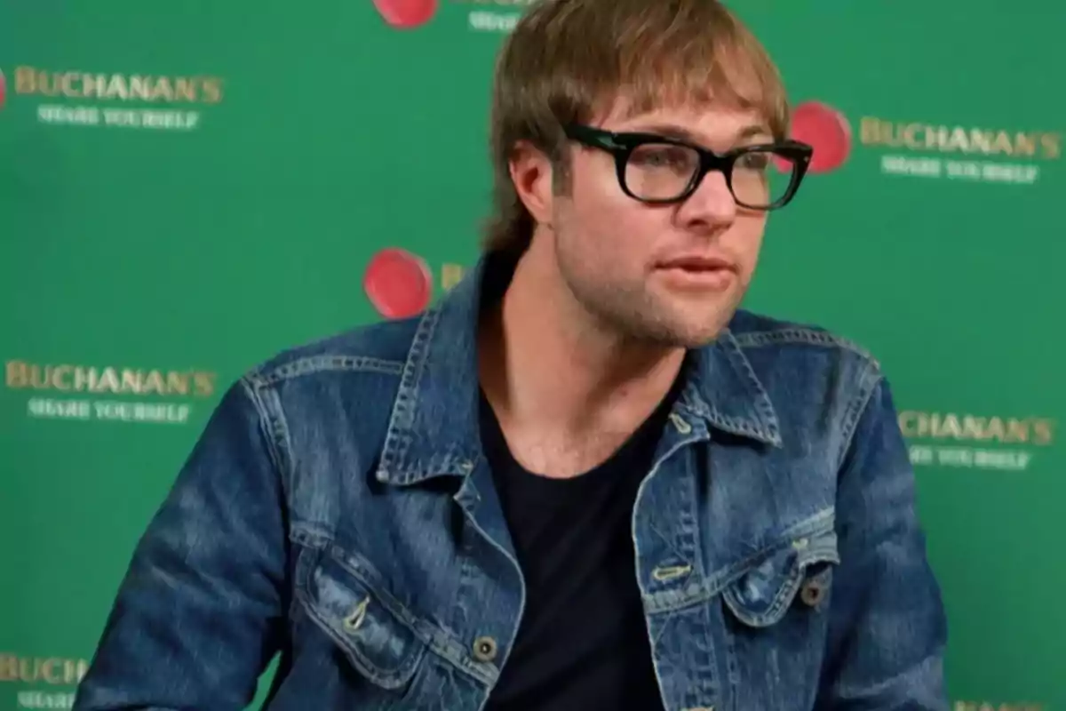 Man with glasses and a denim jacket in front of a green background with Buchanan's logos Man with glasses and a denim jacket in front of a green background with Buchanan's logos