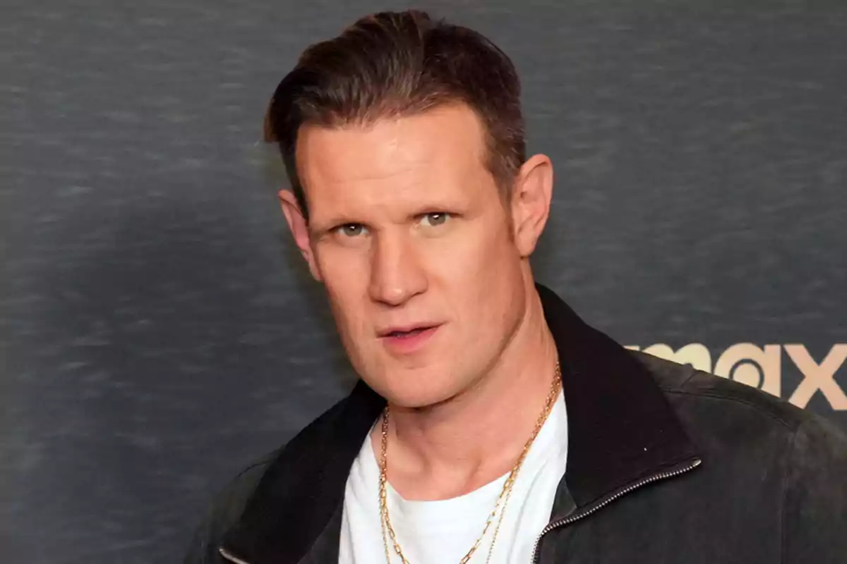 Hombre de cabello corto y oscuro con chaqueta negra y camiseta blanca posando frente a un fondo gris Hombre de cabello corto y oscuro con chaqueta negra y camiseta blanca posando frente a un fondo gris