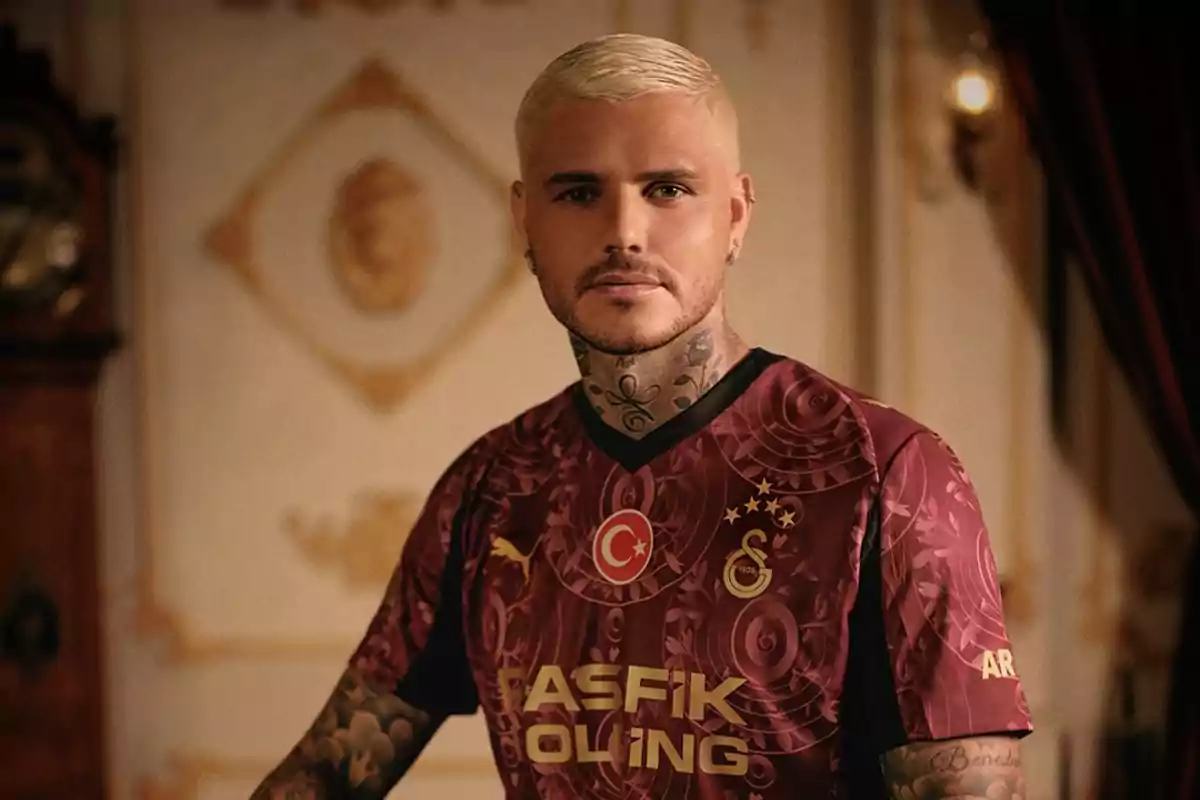 Hombre de cabello rubio y tatuajes vistiendo la camiseta del Galatasaray en una habitación elegante