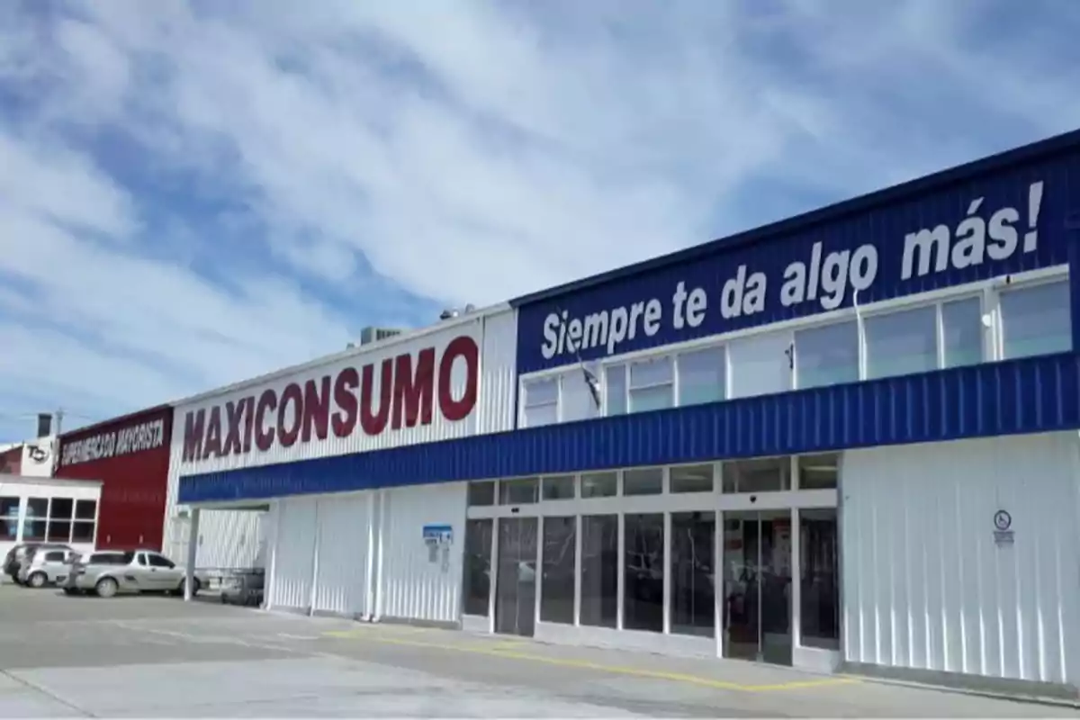 Facade of a Maxi Consumo wholesale supermarket with parked cars and a partly cloudy sky