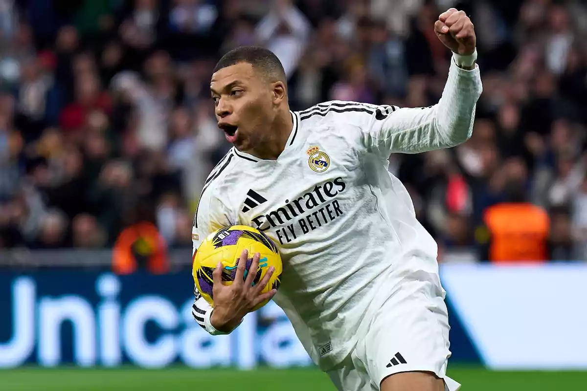 Soccer player in a white uniform celebrating while holding a yellow ball during a match in a stadium full of spectators Soccer player in a white uniform celebrating while holding a yellow ball during a match in a stadium full of spectators