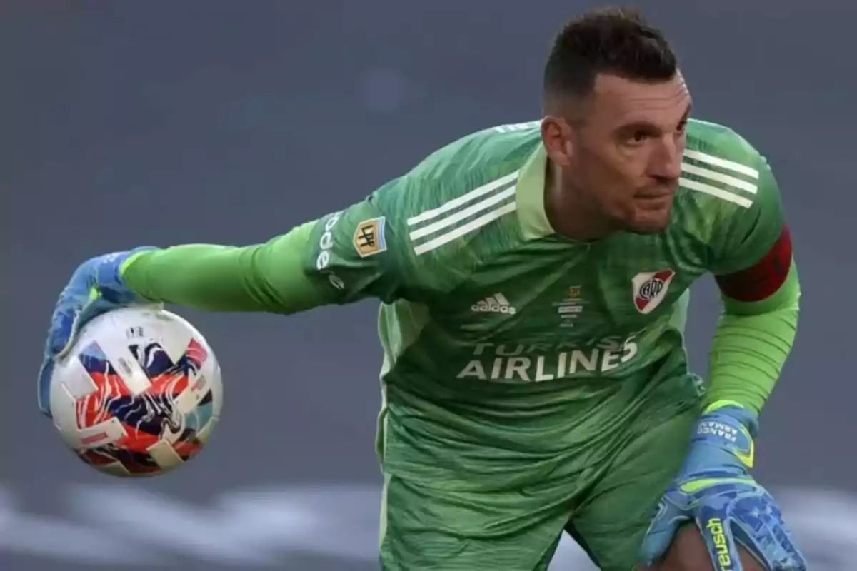 Portero de fútbol con uniforme verde y guantes azules sosteniendo un balón durante un partido