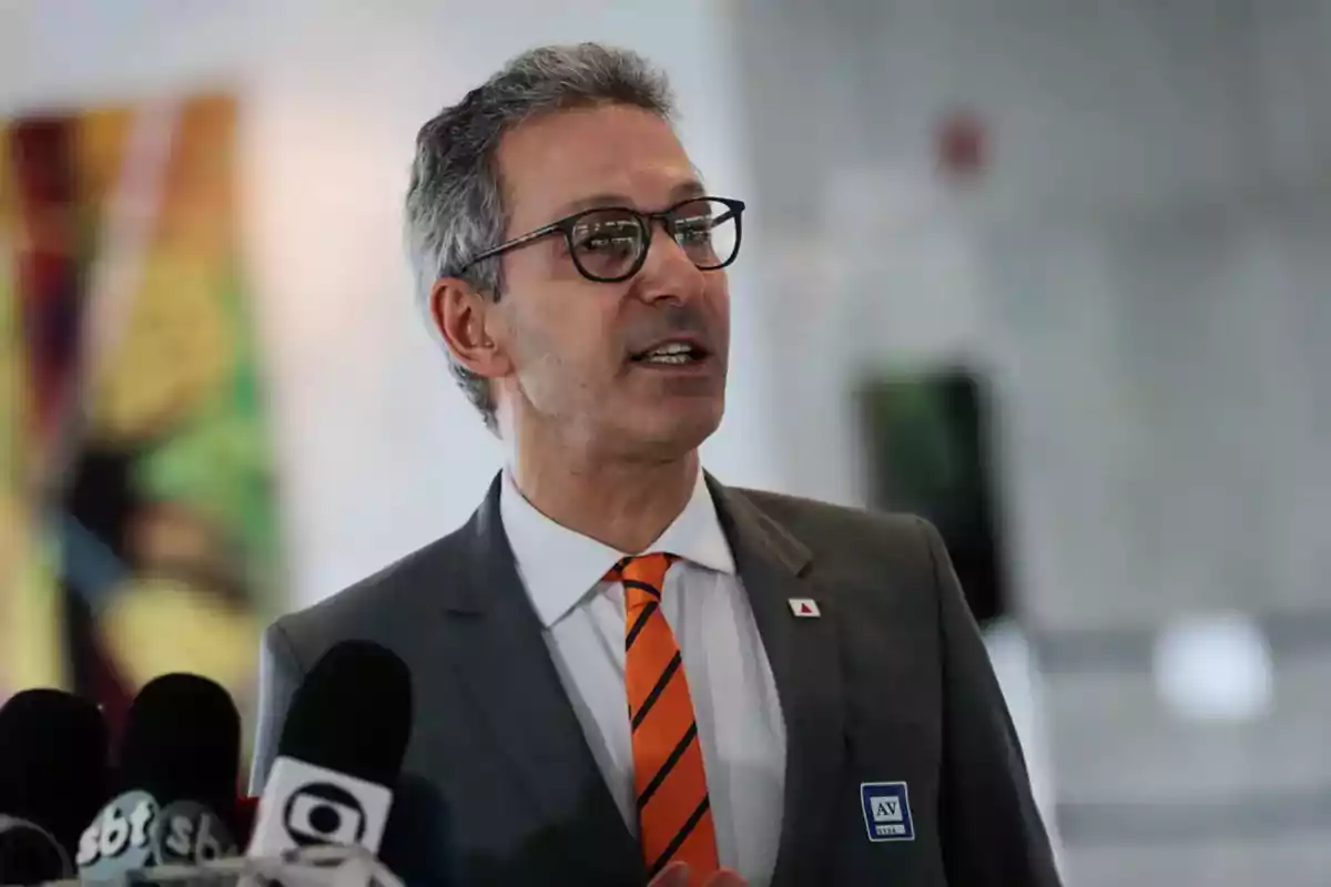 Gray-haired man with glasses speaking in front of several microphones with a blurred background Gray-haired man with glasses speaking in front of several microphones with a blurred background